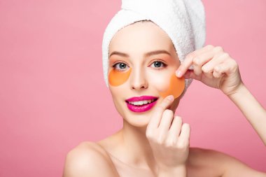 cheerful naked girl applying eye patches isolated on pink 