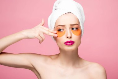 naked girl touching face with eye patches isolated on pink 