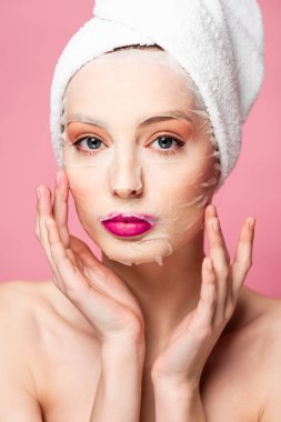 young naked woman in moisturizing face mask touching face isolated on pink 
