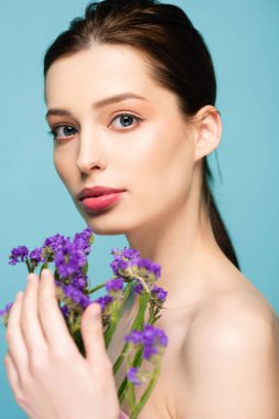 selective focus of pretty girl near limonium flowers isolated on blue 