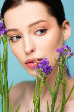 naked woman looking at limonium flowers isolated on blue 