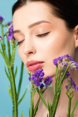 selective focus of naked woman with closed eyes near limonium flowers isolated on blue 