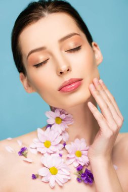 naked young woman with flowers and closed eyes isolated on blue 