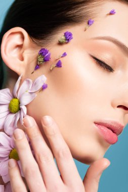 cropped view of young woman with flowers on face isolated on blue 