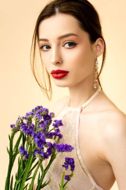 young attractive woman holding limonium flowers isolated on beige 
