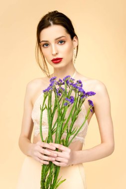 young woman holding purple limonium flowers isolated on beige 