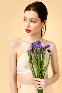 pretty woman holding purple limonium flowers isolated on beige 