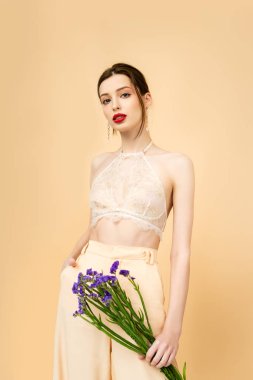 young woman holding limonium flowers and standing with hand in pocket isolated on beige 