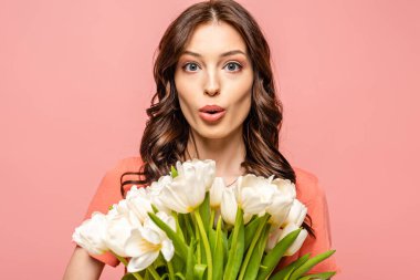 Şaşırmış bir kız, elinde pembe bir buket beyaz lale tutarken kameraya bakıyor.