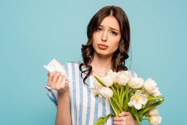 Hastalıklar. Elinde kağıt peçete ve mavi üzerinde izole edilmiş beyaz laleler tutan genç bir kadın.