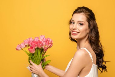 Güzel genç bir kadın kameraya gülümserken elinde sarı renkli bir buket pembe lale tutuyordu.