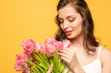 Gülümseyen genç kadın sarı renkli pembe lalelere dokunuyor.