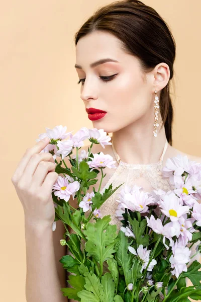 young woman looking at blooming chrysanthemum flowers isolated on beige 