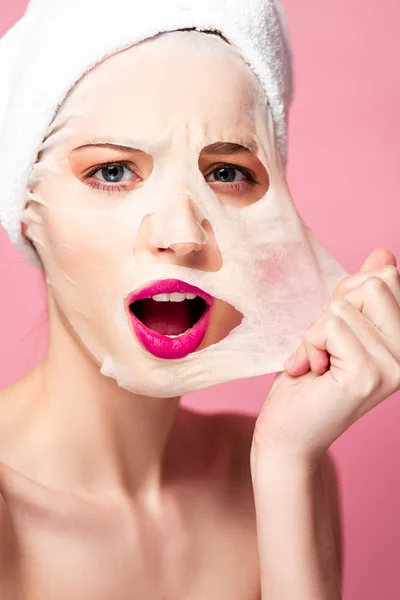 Geschokte Jonge Vrouw Aanraken Gezichtsmasker Geïsoleerd Roze — Stockfoto