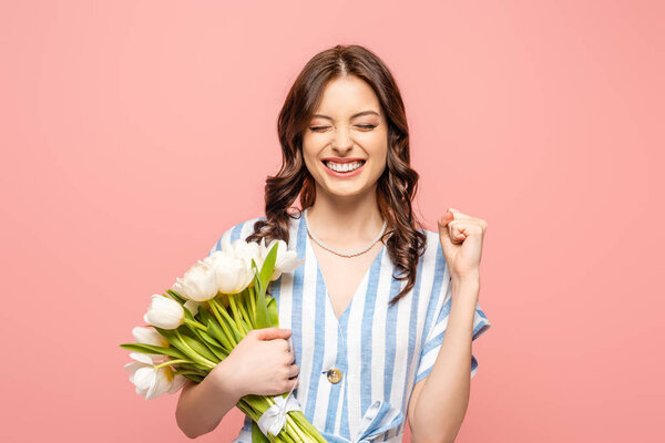 excited girl showing yeah gesture while holding bouquet of white tulips isolated on pink