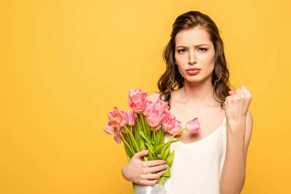 怒った女の子はカメラで拳を見せながらピンクのチューリップの花束を持っています黄色に隔離された — ストック写真