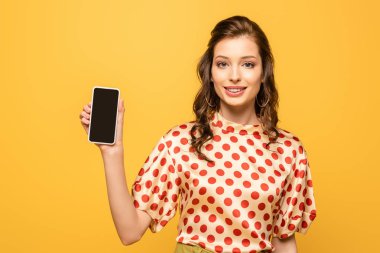 Güzel genç bayan kameraya gülümserken sarı ekranda boş ekranlı akıllı telefon gösteriyor.
