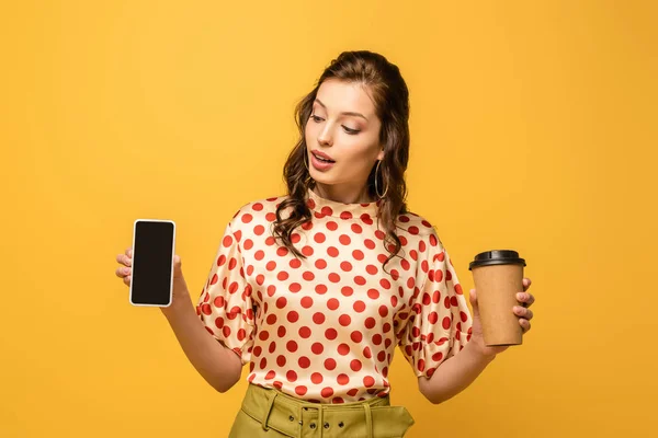 コーヒーを飲みに行く魅力的な若い女性と黄色に隔絶された空白の画面を持つスマートフォン — ストック写真
