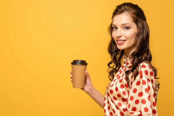 黄色で隔絶されたカメラを見ながらコーヒーを持って行く笑顔の若い女性 — ストック写真