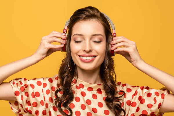 happy young woman listening music in wireless headphones with closed eyes isolated on yellow