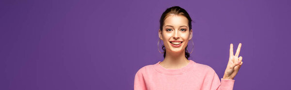 панорамный снимок счастливой девушки, показывающей победный жест, изолированный на фиолетовый
