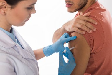 Selective focus of doctor doing injection with vaccine in shoulder of patient isolated on white clipart