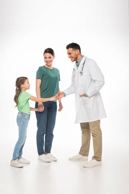 Gülümseyen bir çocuk doktoru, beyaz arka planda annesinin yanındaki çocukla tokalaşıyor.