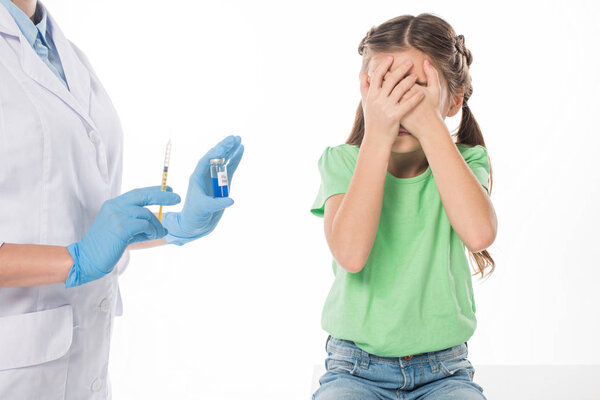 Pediatrician with syringe and flu vaccine near scared kid isolated on white