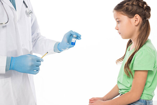 Side view of pediatrician holding flu vaccine and syringe near kid isolated on white