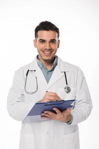 Guapo Doctor Sonriendo Cámara Blanca Escritura Portapapeles Aislado Blanco — Foto de Stock