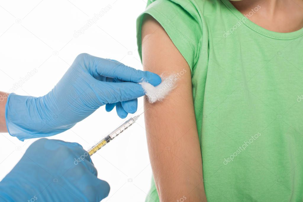 Cropped view of pediatrician holding cotton wool and syringe while doing vaccine injection to kid isolated on white