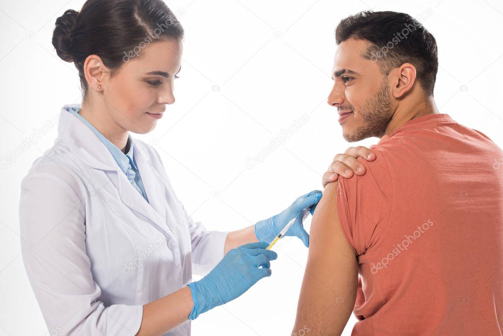 Smiling patient looking at doctor doing vaccine injection isolated on white