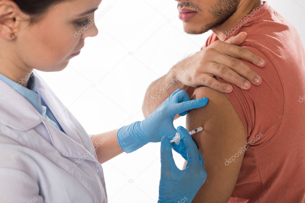 Selective focus of doctor doing injection with vaccine in shoulder of patient isolated on white