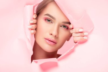 Güzel bir kız yırtık bir kağıtta mükemmel cilde sahip, pembe renkte izole edilmiş.