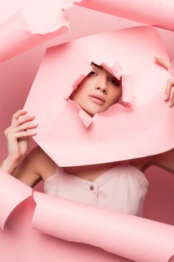 Pembe elbiseli çekici bir kadın yırtık kağıtlarla poz veriyor, pembe.