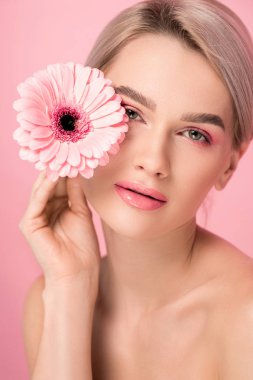 Pembe makyajlı hassas çıplak kadın elinde Gerbera çiçeği, pembe üzerine izole edilmiş.