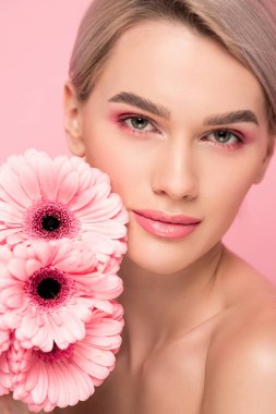 Pembe Gerbera çiçekleri olan güzel genç bir kadın, pembe üzerine izole edilmiş.