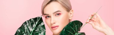 panoramic shot of attractive girl with pink makeup isolated on pink with green leaves  clipart