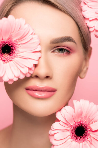 beautiful girl with pink makeup and gerbera flowers, isolated on pink