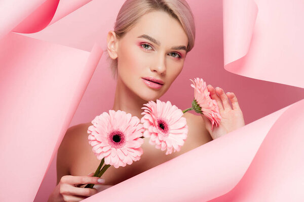 attractive girl with pink flowers and makeup in torn paper, on pink