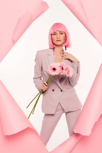 魅力的なスタイリッシュな女の子スーツとピンクのウィッグの花を保持し 白い上に隔離された引き裂かれた紙にポーズ — ストック写真