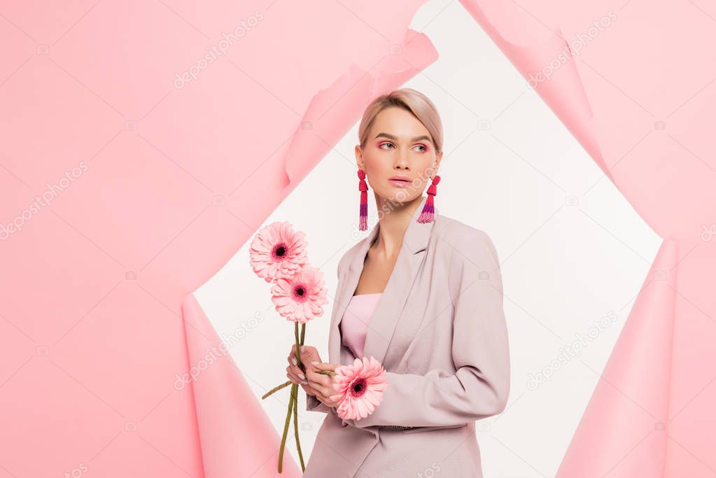 attractive blonde girl in stylish suit holding flowers and posing in torn paper, isolated on white