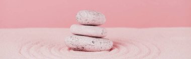 Kum yüzeyindeki Zen taşlarının panoramik görüntüsü pembe arkaplanda daireler çiziyor.