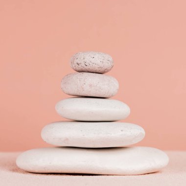 Close up view of stacked zen stones on sand isolated on peach  clipart