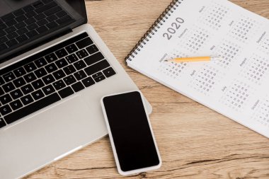 Ahşap arkaplanda kurşun kalemle takvim yakınında boş ekranlı akıllı telefon