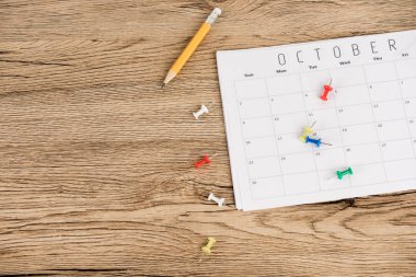 Top view of pencil, office pins and calendar of October on wooden surface clipart