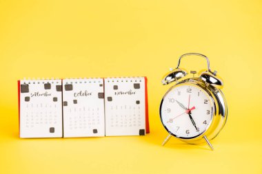 Alarm clock and calendar with autumnal months on yellow background clipart