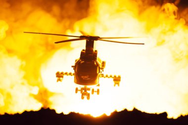 Oyuncak helikopterle savaş sahnesi ve arka planda yangın