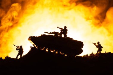 Oyuncak tank ve arka planda ateş olan askerlerin savaş sahnesi