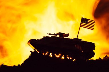 Battle scene with american flag on toy tank and fire at background clipart